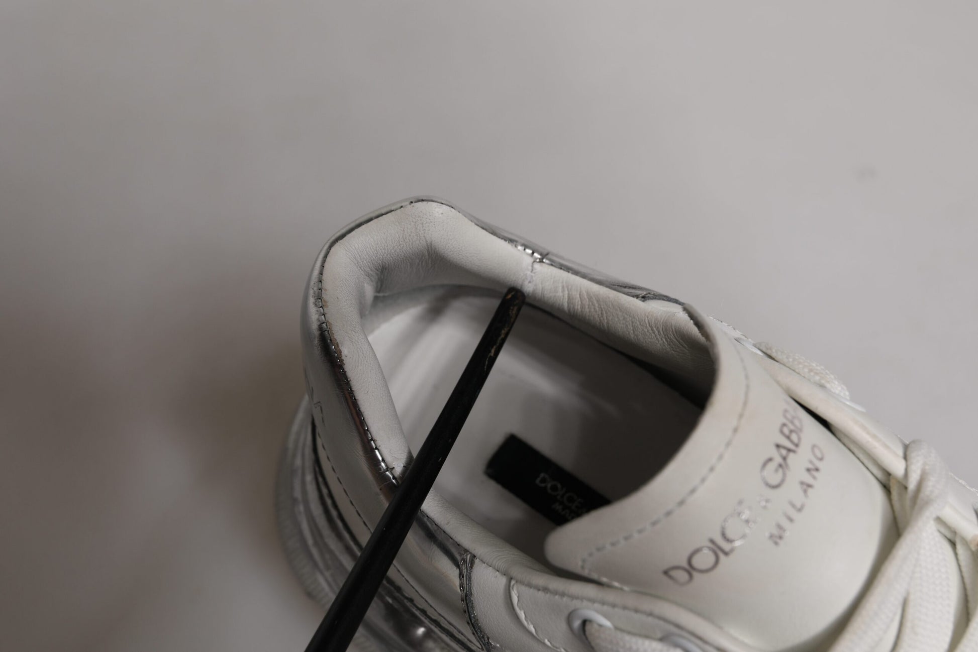 A white and silver sneaker with a low top, featuring the Dolce & Gabbana logo