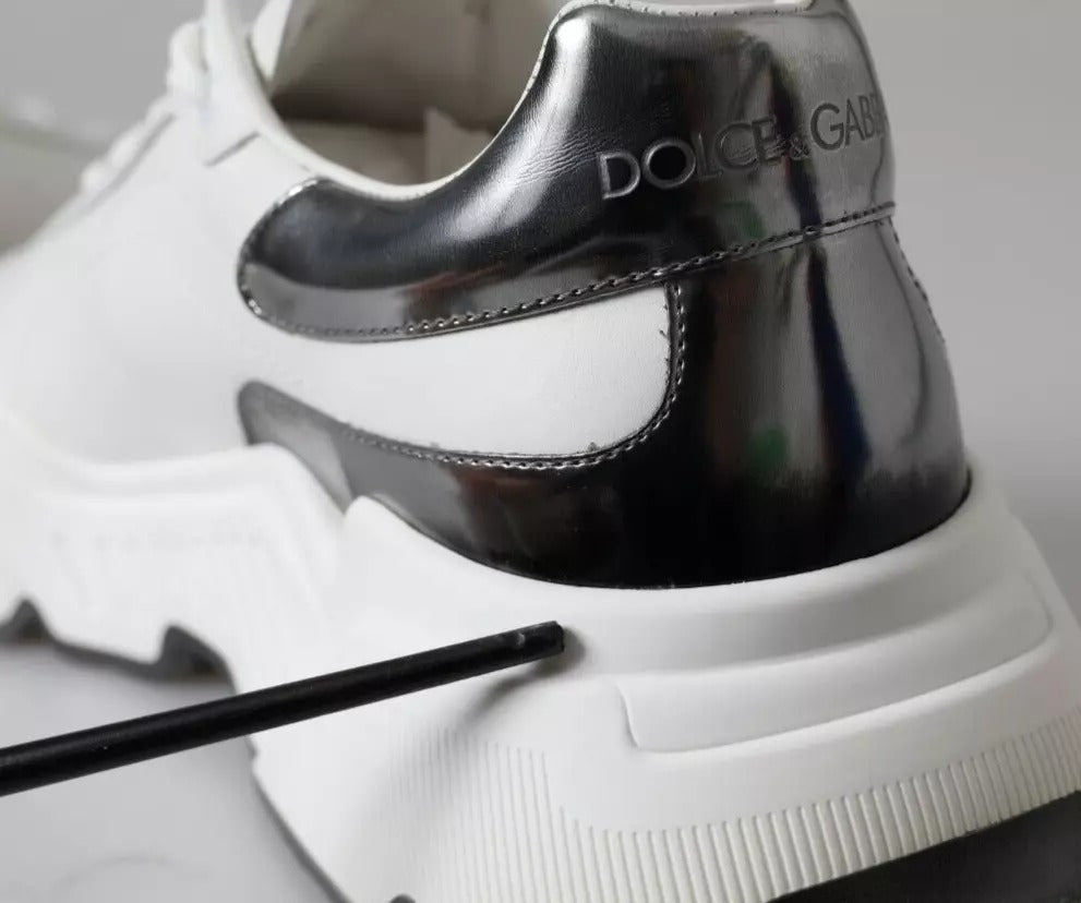 A pair of white and silver leather sneakers with a black logo on the side