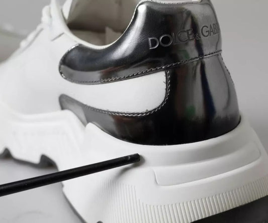 A pair of white and silver leather sneakers with a black logo on the side