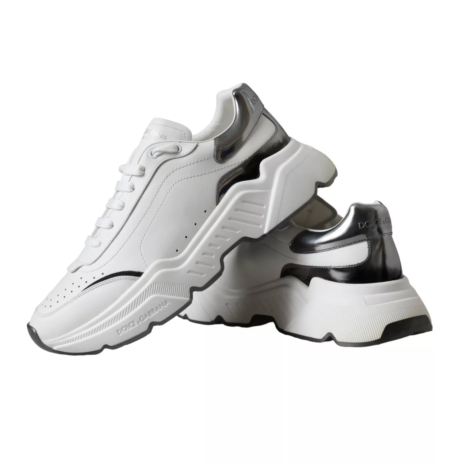 Pair of white sneakers with black accents, featuring a silver leather upper and chunky soles