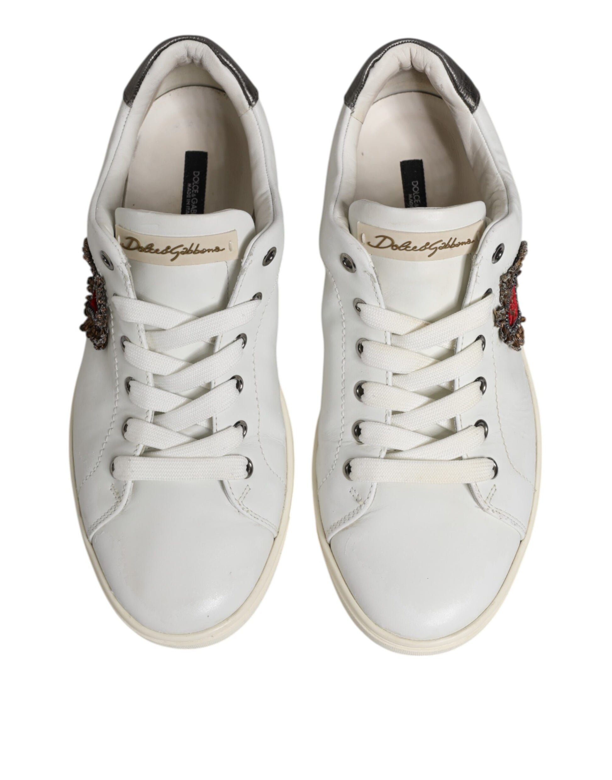Pair of white sneakers with silver accents, featuring a sacred heart logo on the side