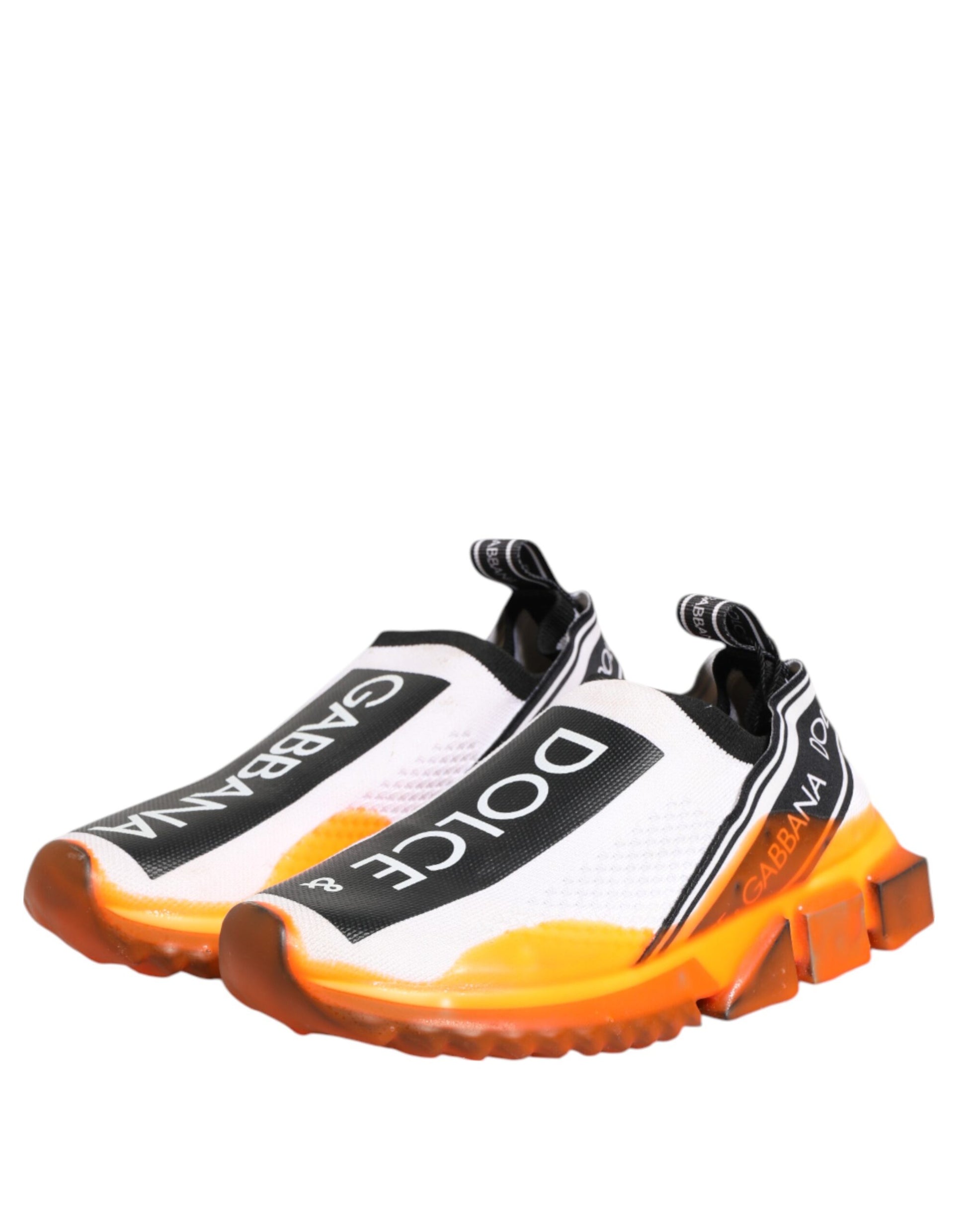A pair of white slip-on shoes with black and orange accents, featuring the brand name "Dolce & Gabbana" on the side