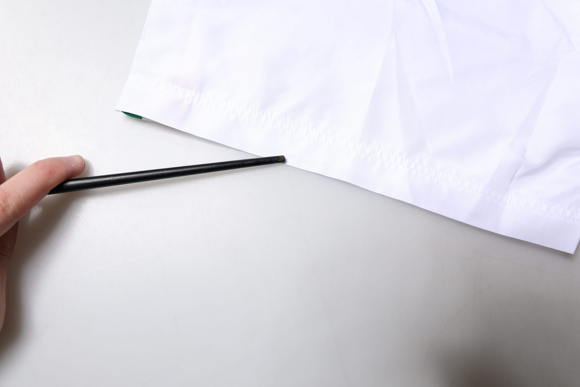Hand holding black pen over white swim shorts with stripes