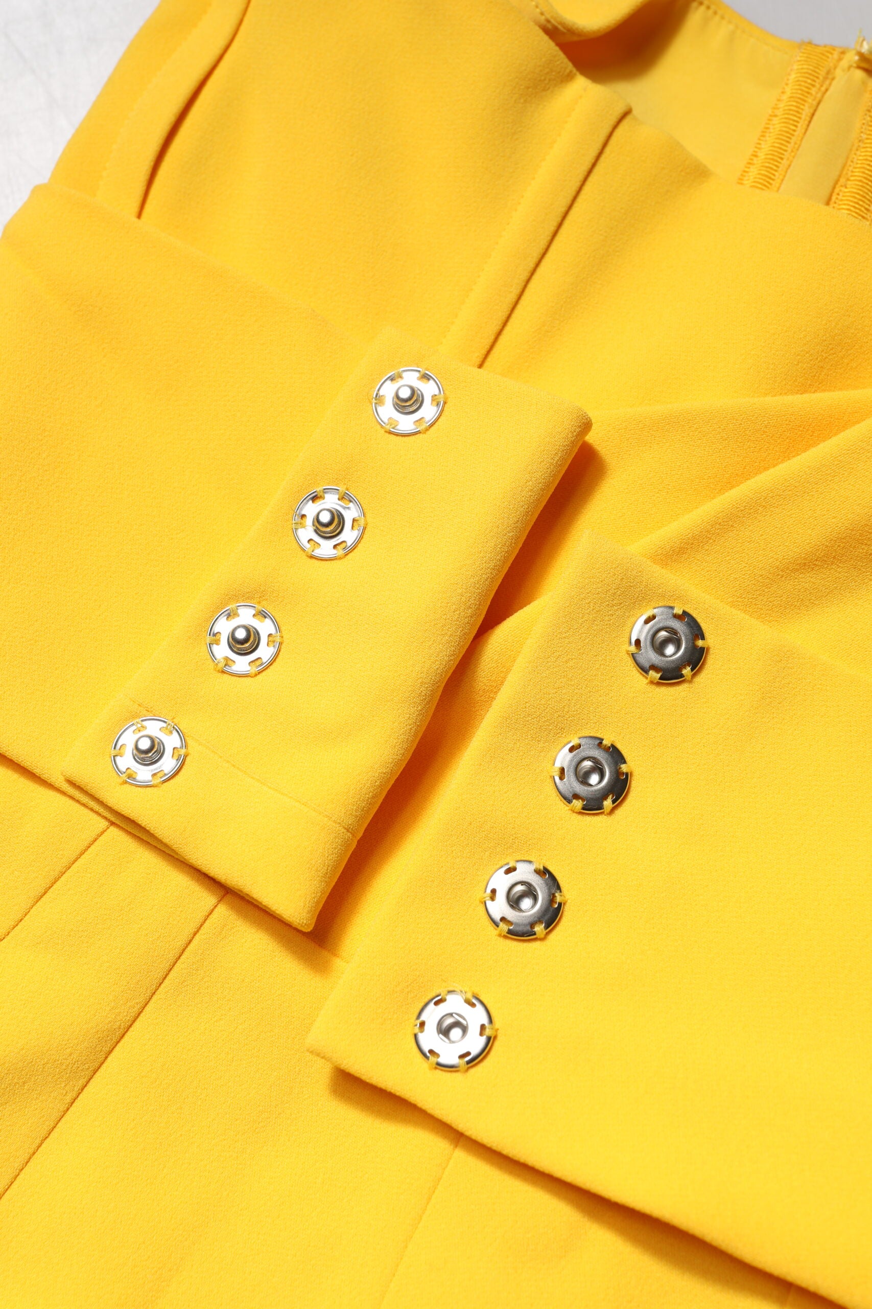 A yellow midi dress with a side slit and one shoulder, featuring silver buttons down the front