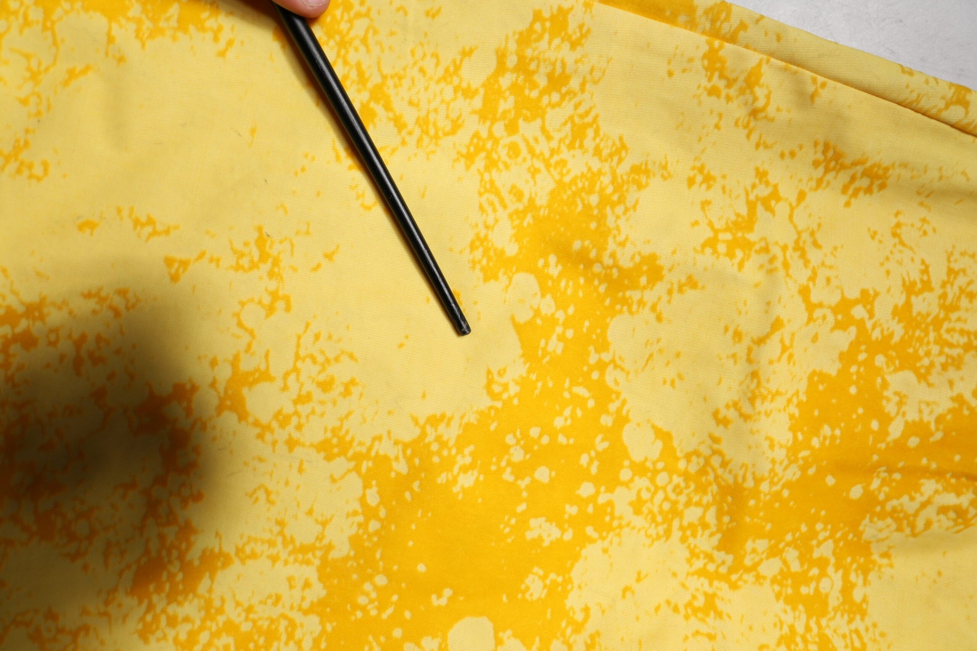 Hand holding black paintbrush over yellow fabric with spots