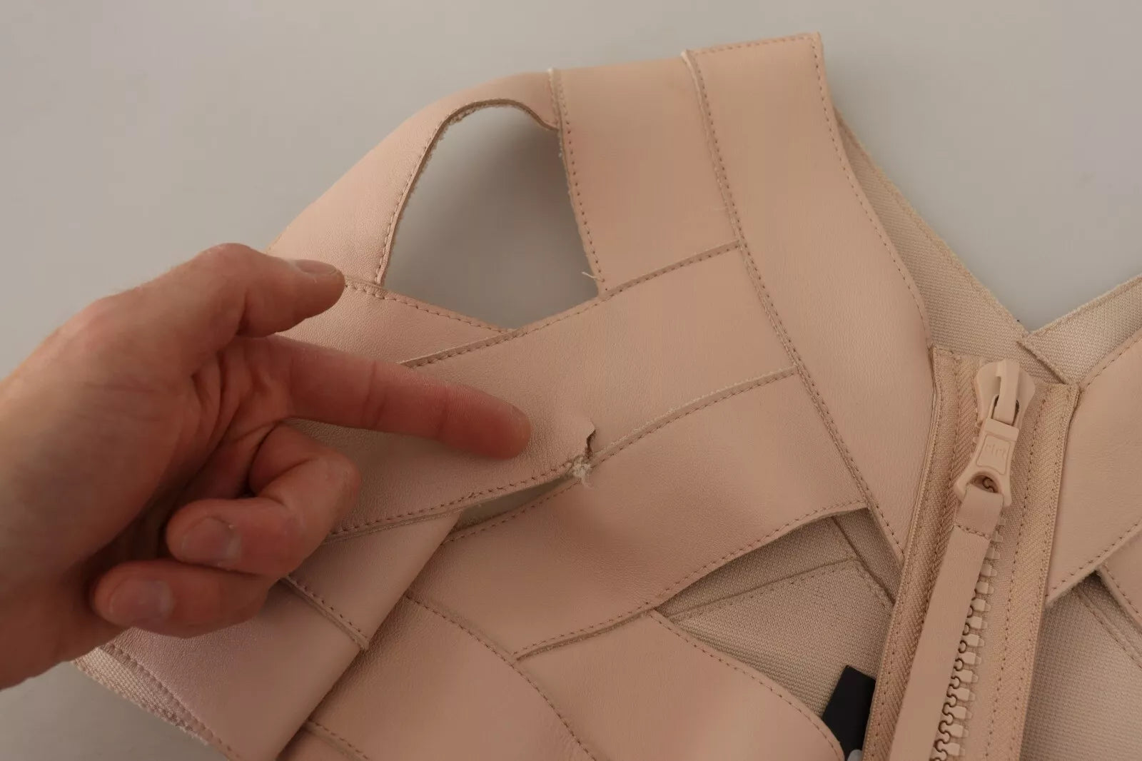 A beige leather open shoulder sheath mini dress with a zipper on the front