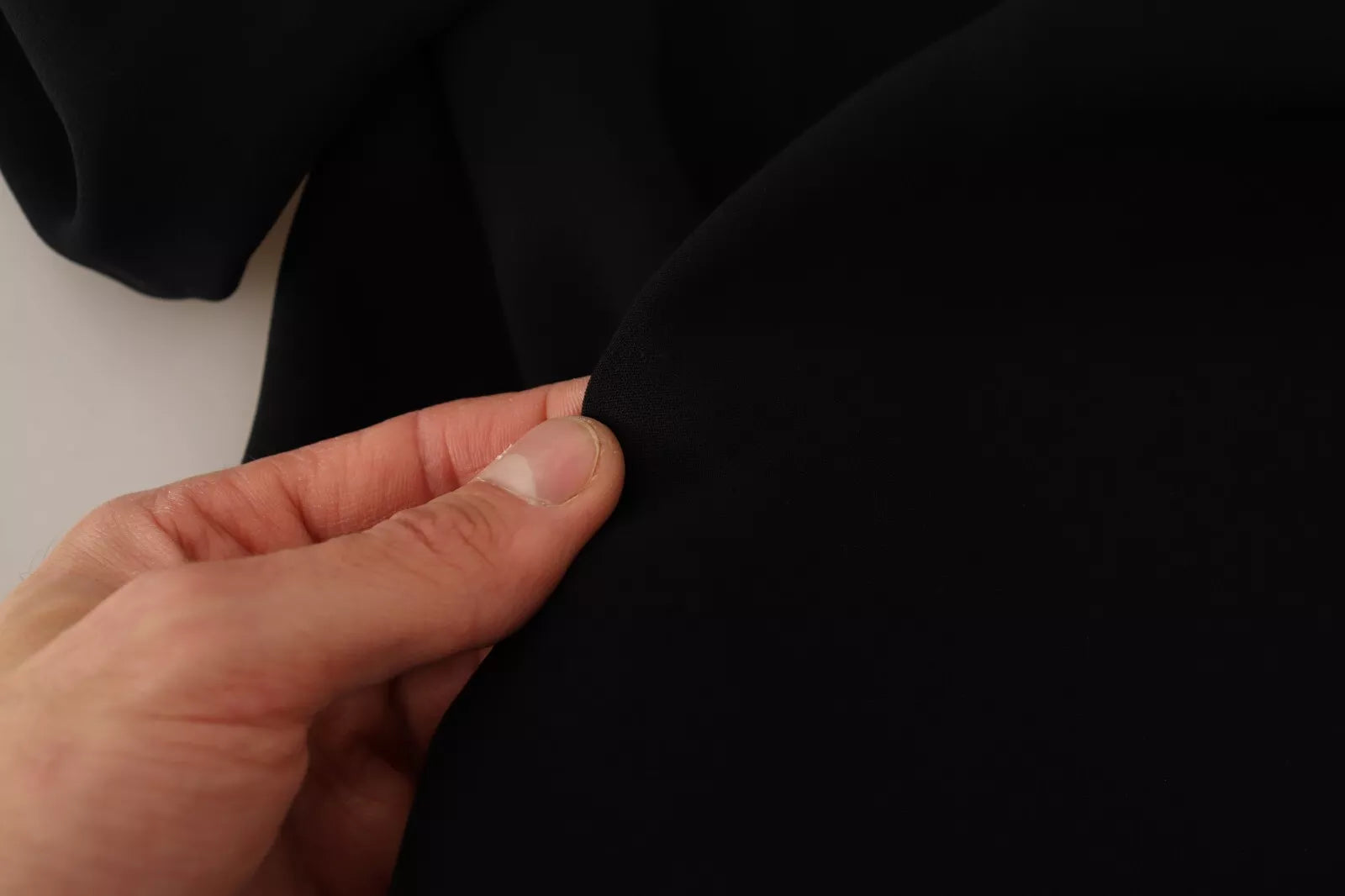 A person's hand is holding a black dress with side slits and long sleeves