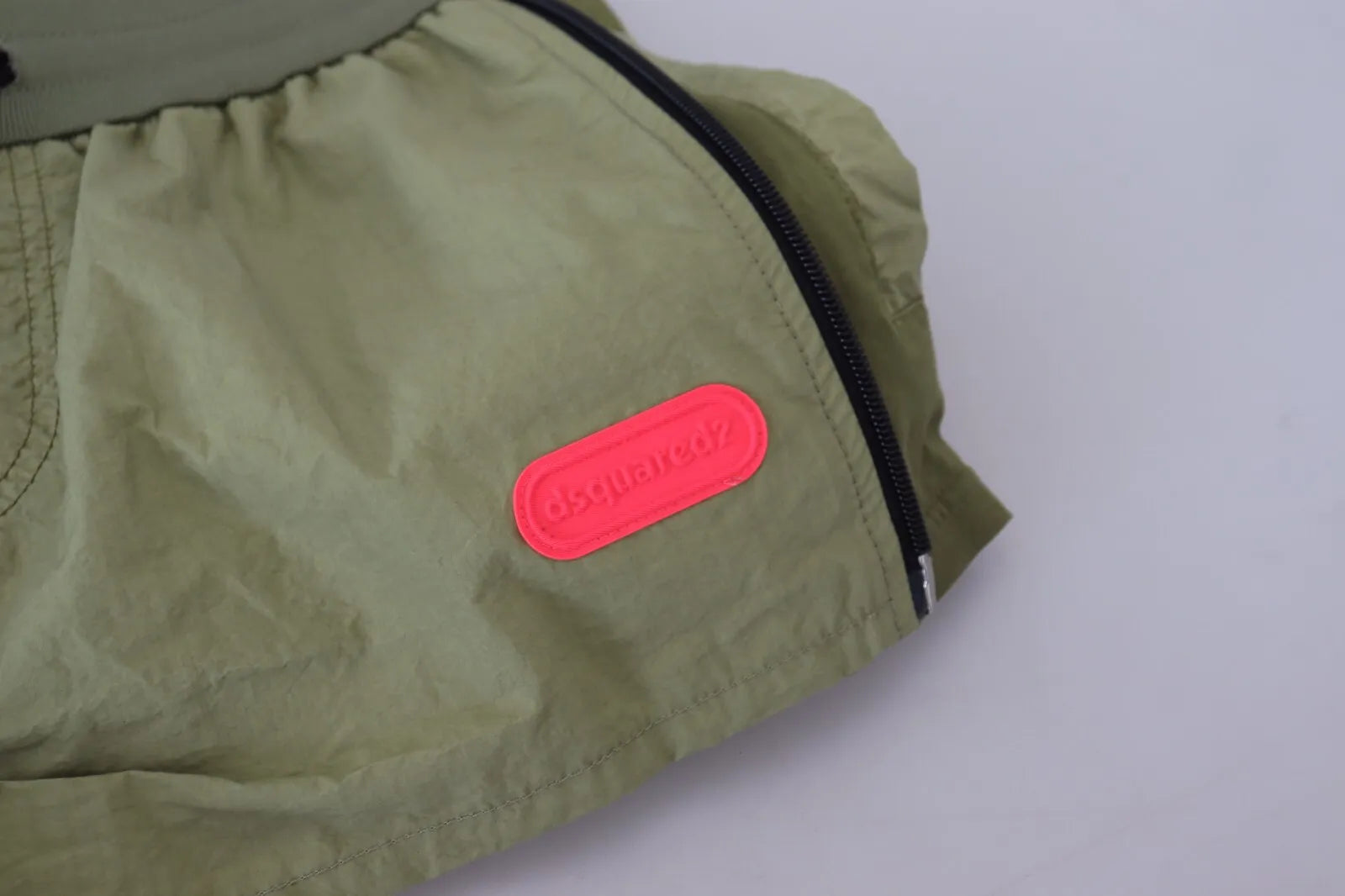 A pair of green cotton shorts with a drawstring waist and tapered legs, featuring a red logo on the left leg