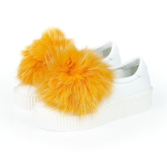 A pair of white sneakers with yellow fur pom poms on the heels