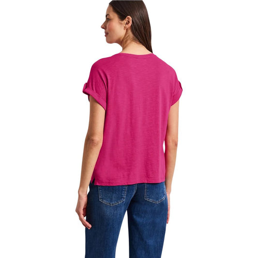 A pink cotton t-shirt with short sleeves, worn by a woman standing against a white background