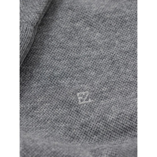A close-up view of a gray fabric item, possibly a sweater or shirt, with a small embroidered logo on the left
